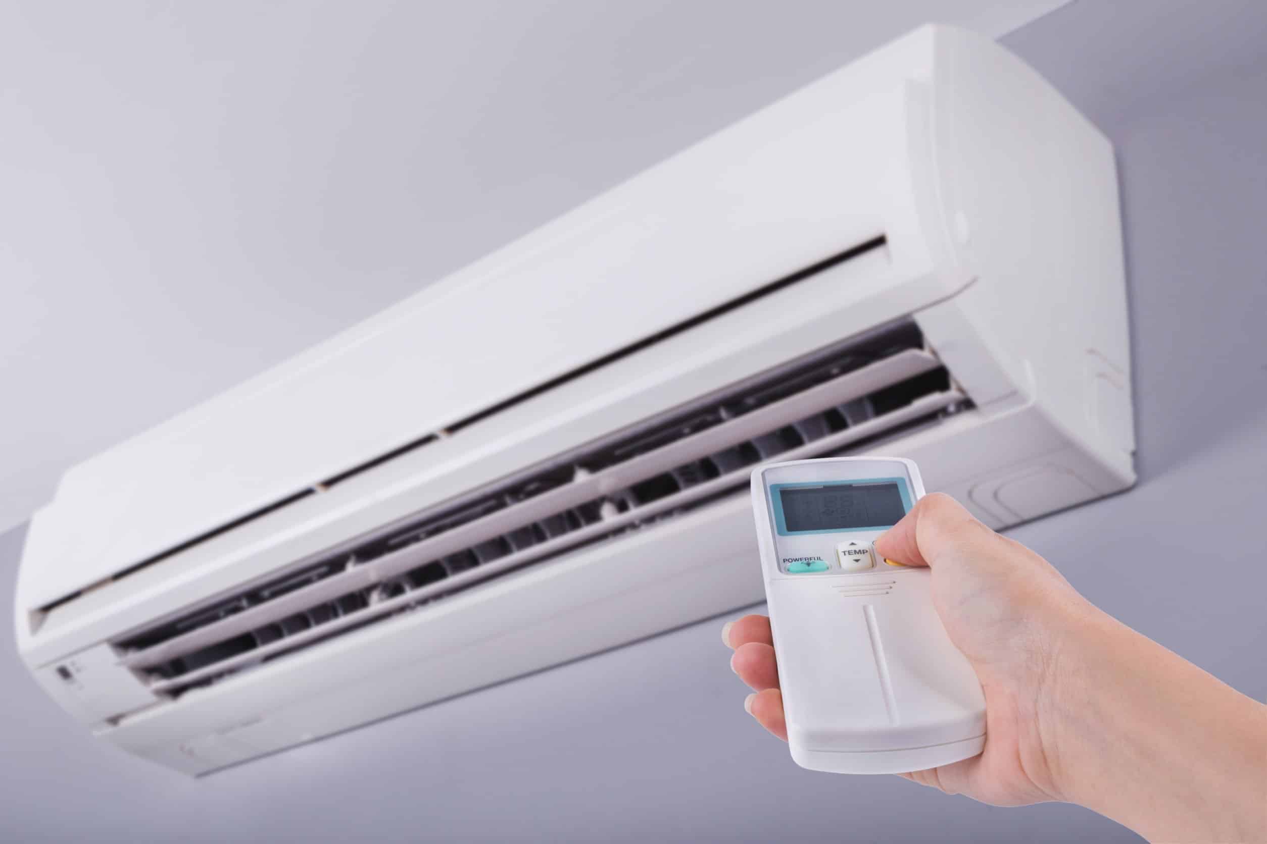 A hand pointing a remote at a ductless AC system